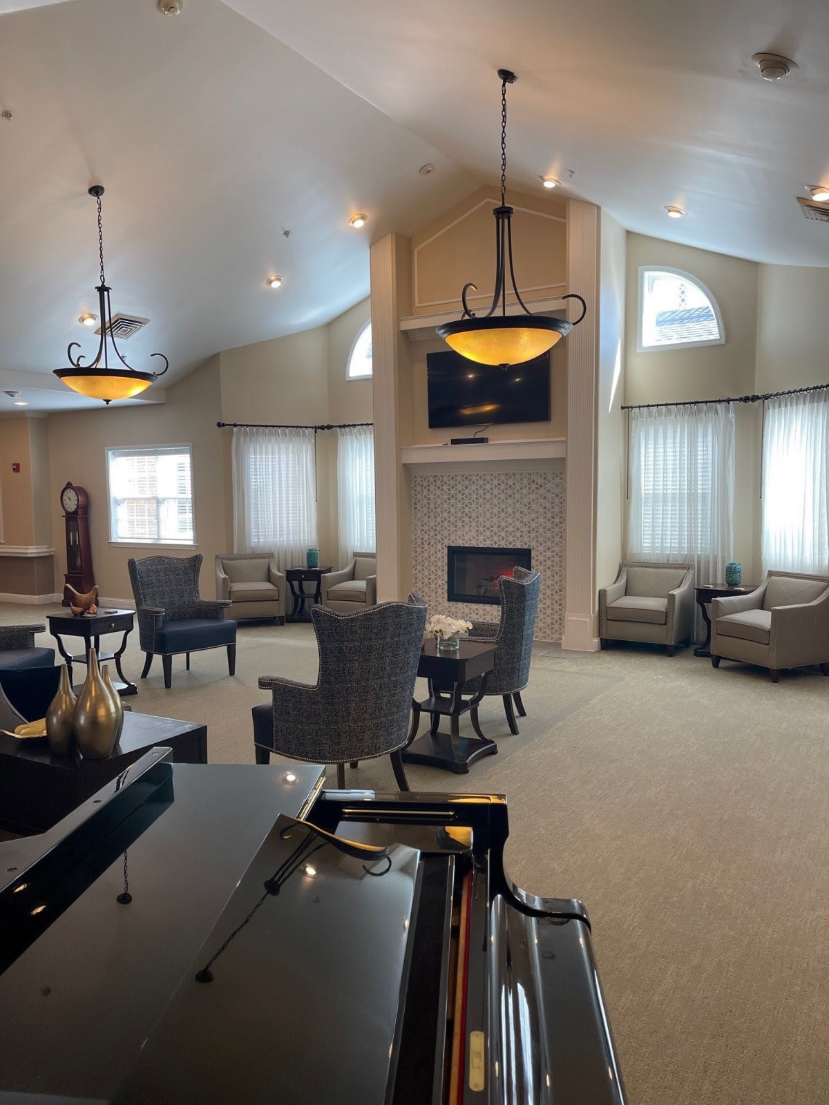 A spacious living room with elegant furniture, a fireplace, and a grand piano under stylish chandeliers.