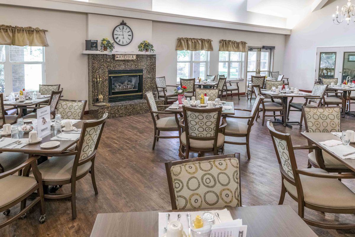 A well-arranged dining area with wooden flooring, featuring elegant chairs and tables, a fireplace, and large windows.