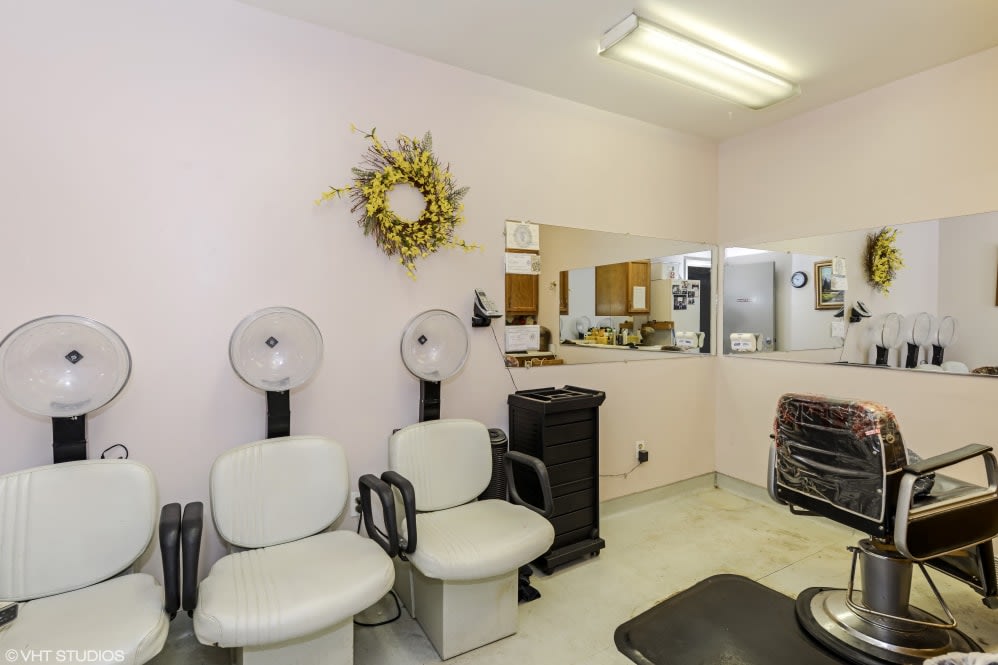 A cozy salon interior with chairs and hair dryers, featuring a mirrored wall and decorative wreath.