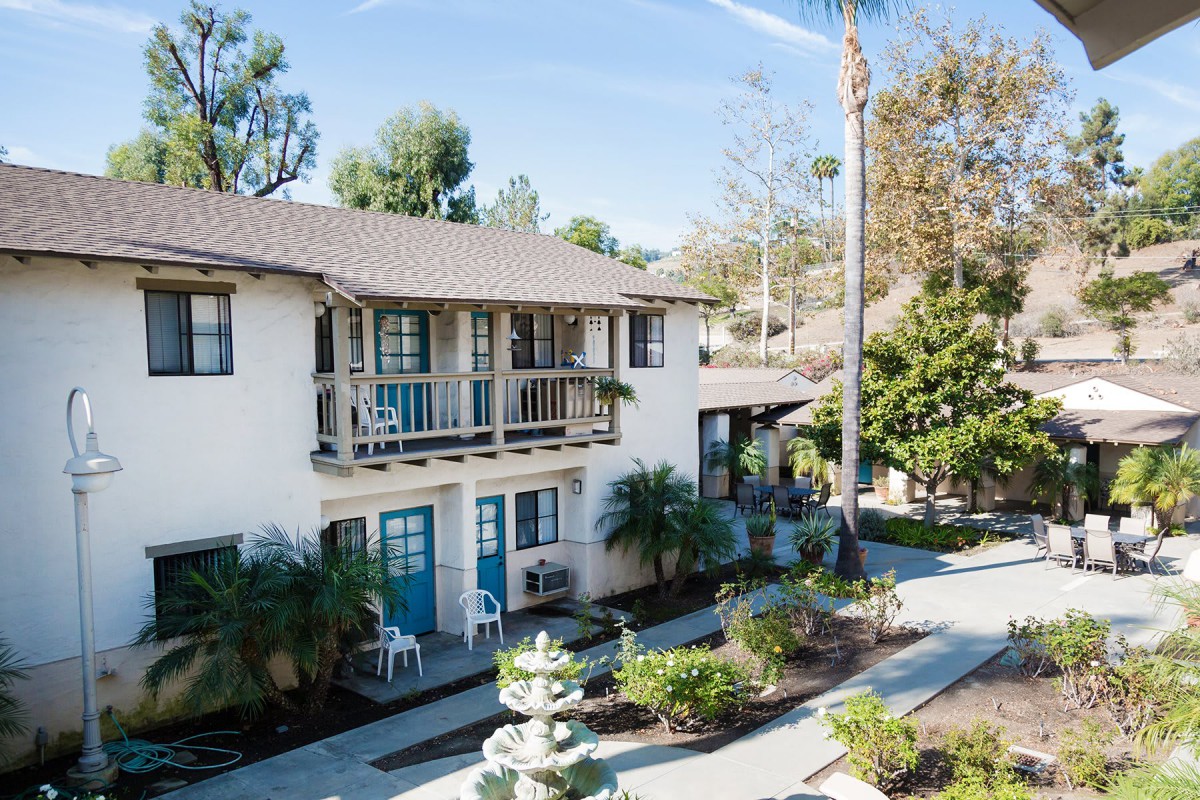 A sunny view of a two-story apartment building with balconies and a landscaped garden.