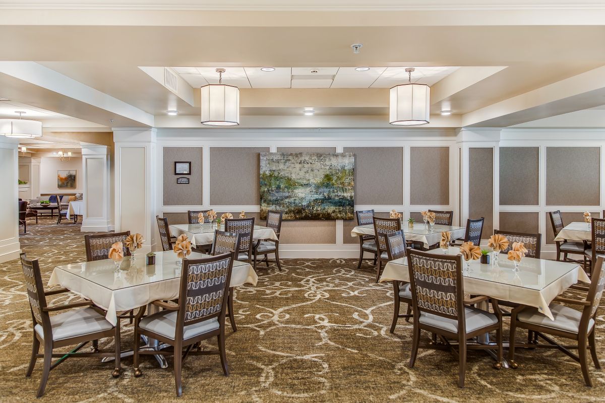 A well-decorated dining room with several tables and chairs, featuring elegant chandeliers and artwork on the walls.