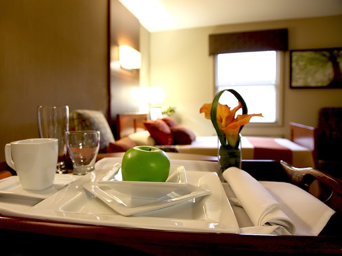 A cozy hotel room with a tray featuring an apple, glassware, and flowers on the side table.