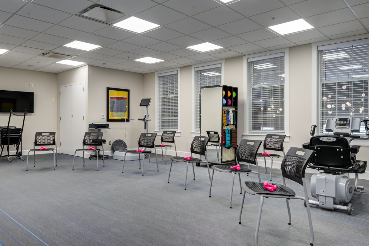An empty, modern waiting room with chairs arranged in rows and large windows providing natural light.