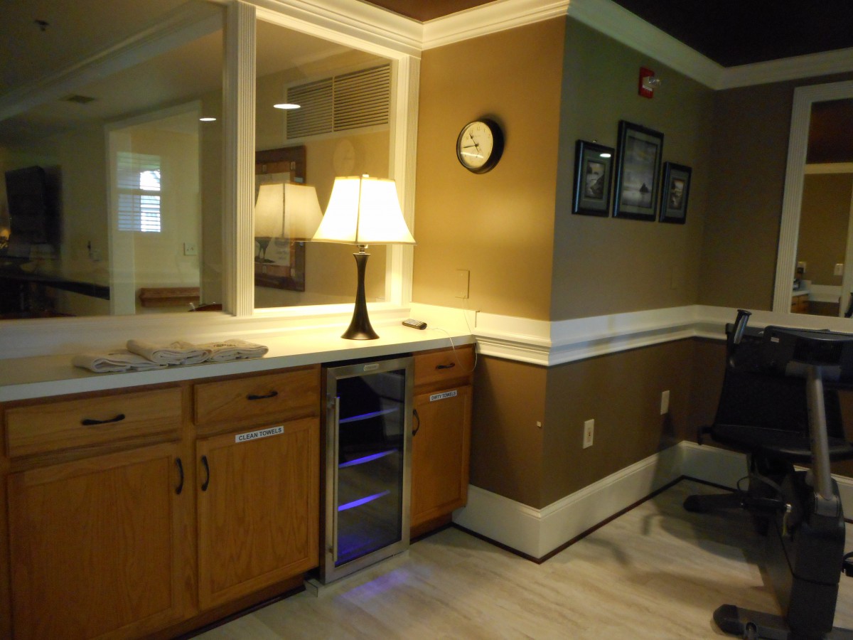 A cozy office interior featuring a desk with a lamp, a small fridge, and framed pictures on the wall.