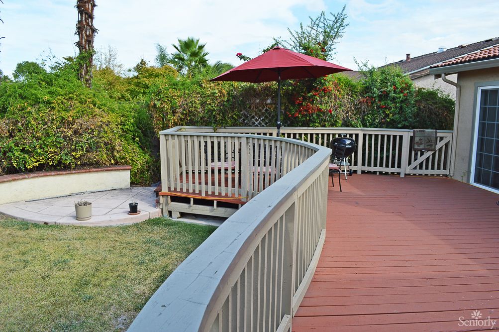A cozy outdoor deck with a red umbrella and surrounding garden.
