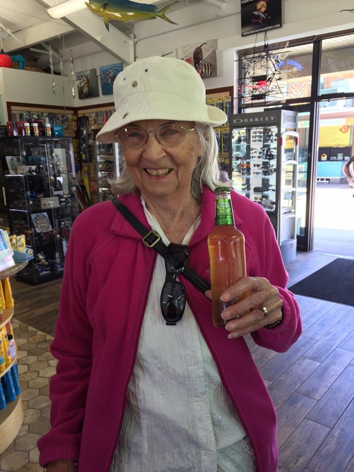 A woman wearing a hat and glasses smiles while holding a bottle in a store.