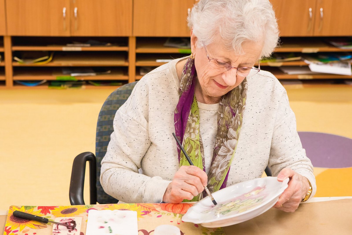 An elderly woman engaging in a painting activity indoors.