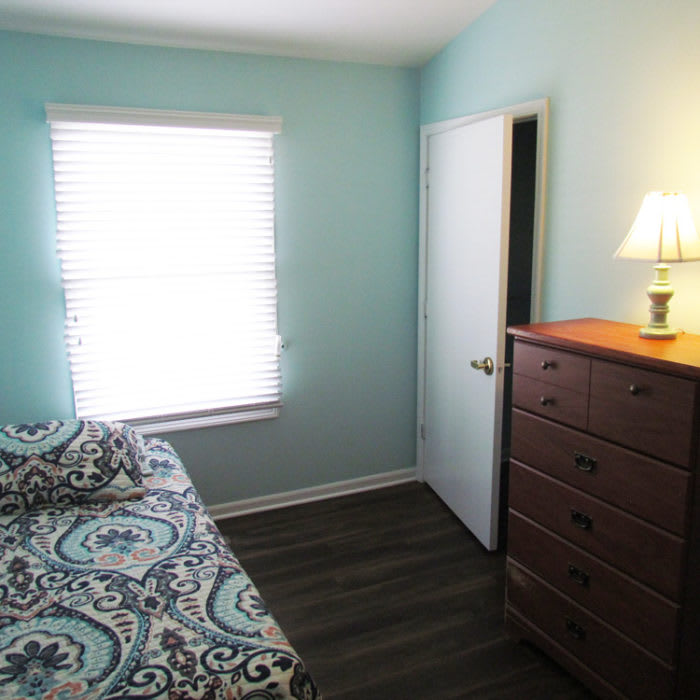 A cozy bedroom with a bed, dresser, and a window letting in natural light.