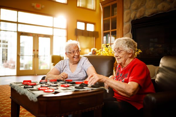 Two elderly women enjoying a game of checkers together indoors.