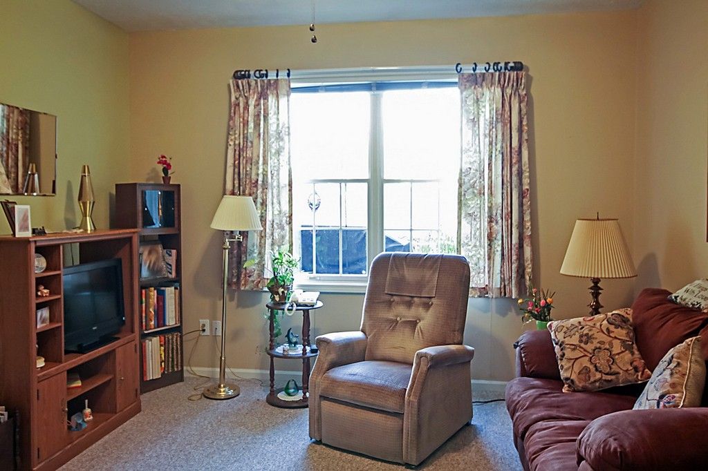 A cozy living room with a recliner, bookshelf, and window with curtains.