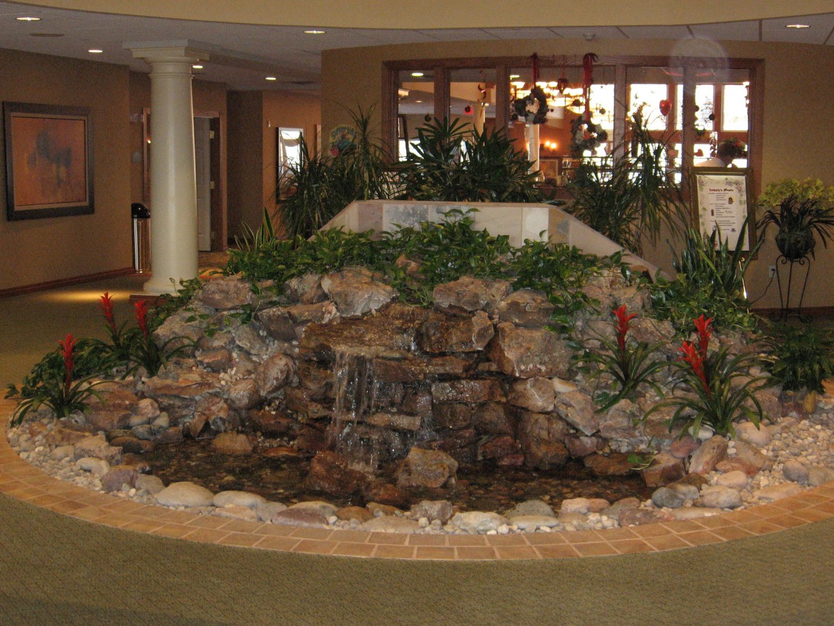 An indoor waterfall with rocks and lush greenery in a well-lit interior setting.