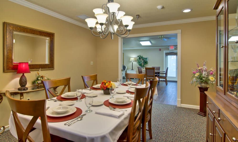 A neatly arranged dining room with a large table set for dinner under a chandelier.