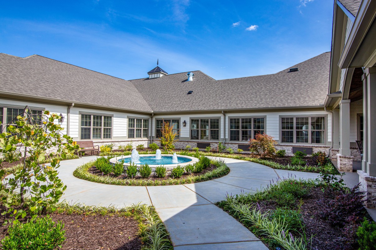 A beautifully landscaped courtyard with a central fountain surrounded by pathways and a building in the background.