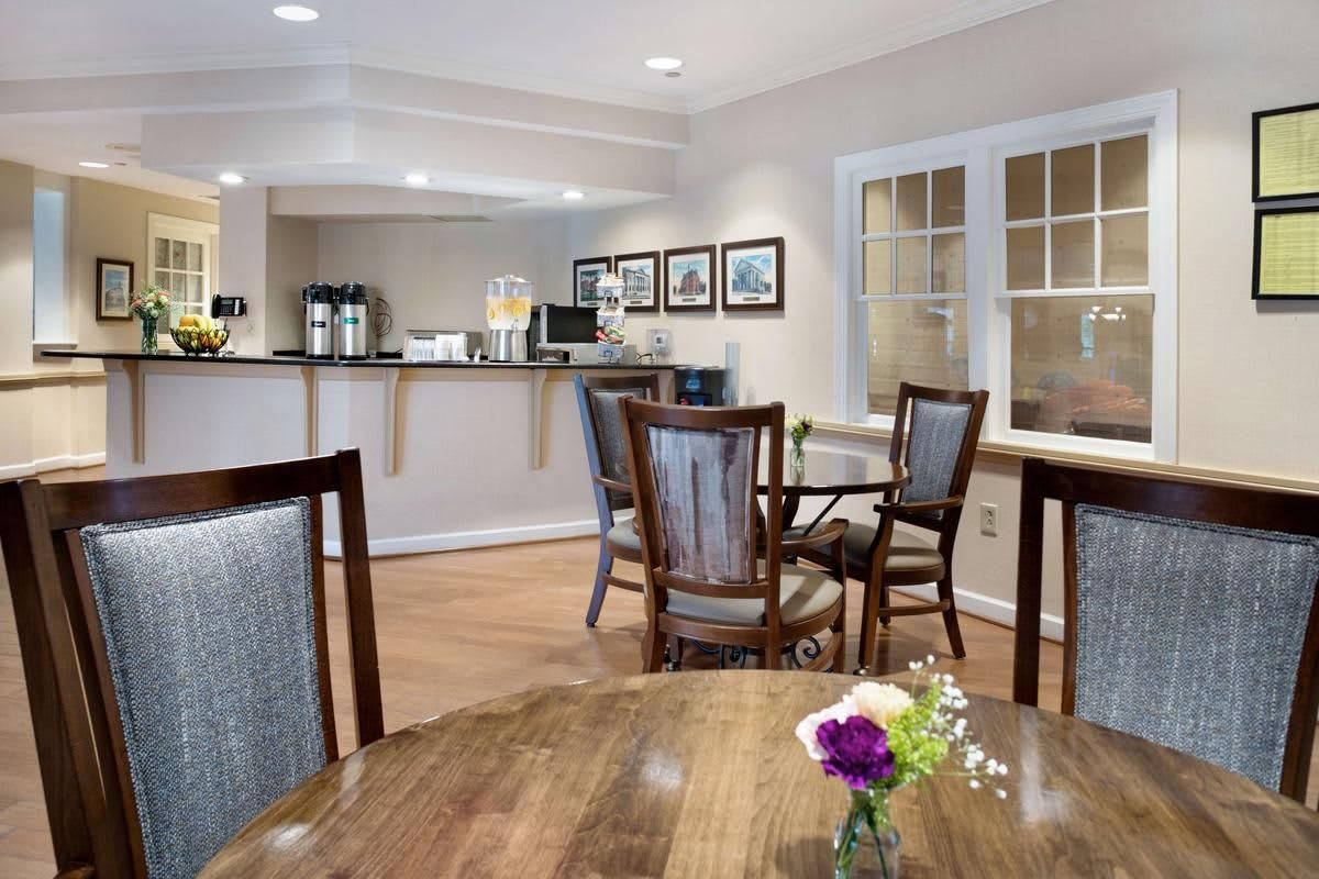 A cozy dining area with wooden tables, chairs, a coffee station, and decorative flowers.