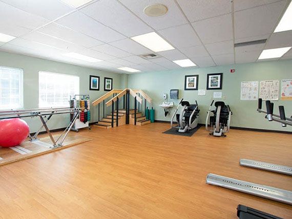 A bright and spacious fitness room equipped with exercise machines and rehabilitation equipment.