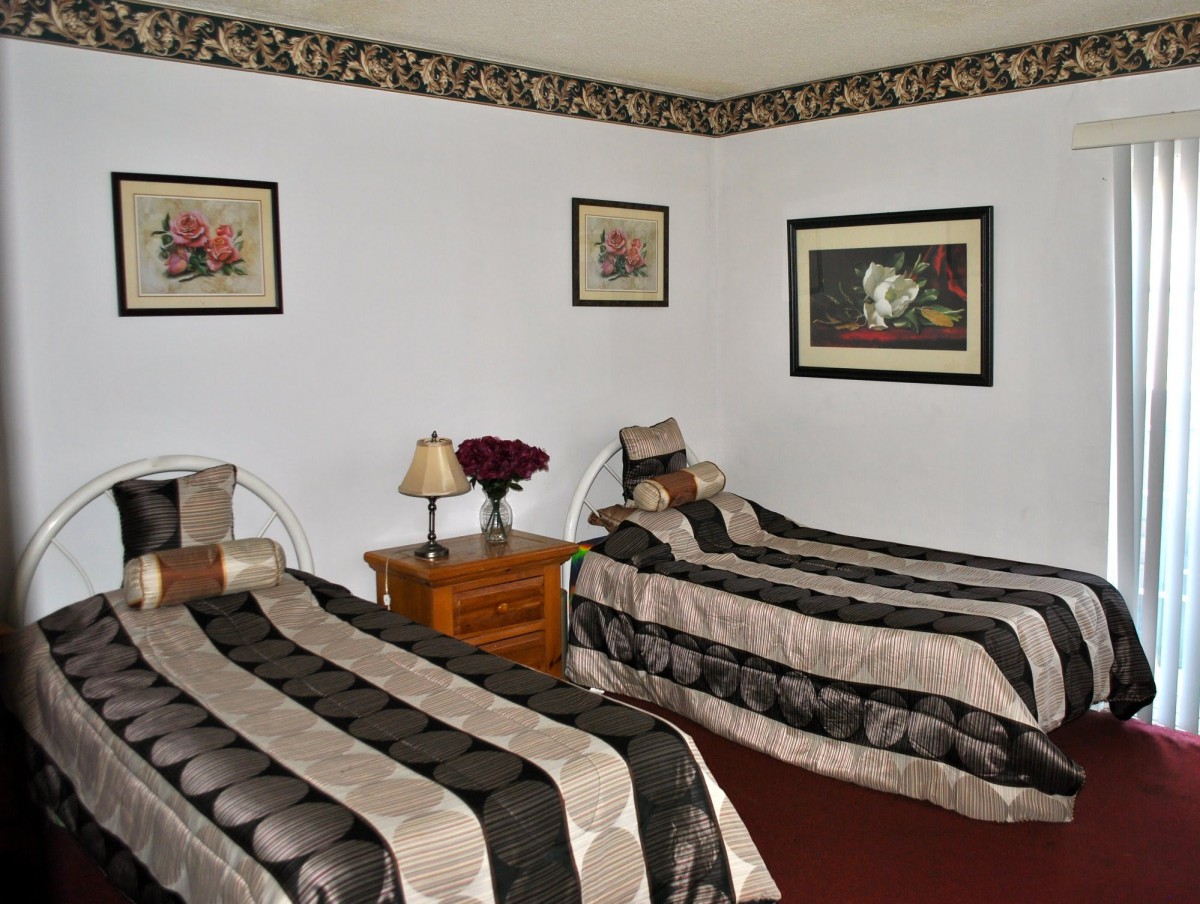 A cozy bedroom featuring two twin beds with matching bedspreads, complemented by framed artwork and a wooden nightstand.