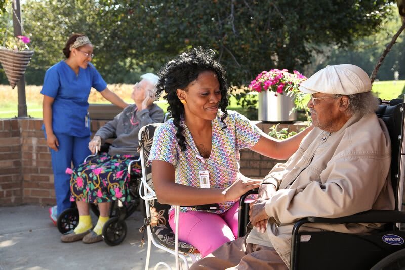 A caregiver interacts warmly with an elderly man in a garden setting, promoting a caring environment.