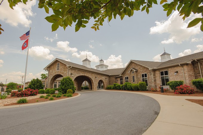 A large stone building with a circular driveway and neatly maintained landscaping beneath a cloudy sky.