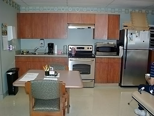 A modern kitchen featuring wooden cabinets, stainless steel appliances, and a small dining area.