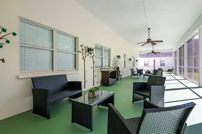 A modern outdoor patio with comfortable seating, green flooring, and a ceiling fan for ventilation.