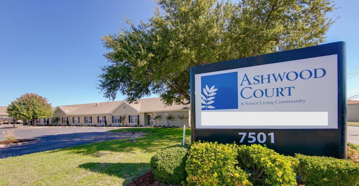 A sign in front of a building with trees and grass on a clear day.