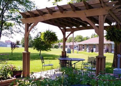A serene outdoor patio with a wooden pergola providing shade over garden furniture.