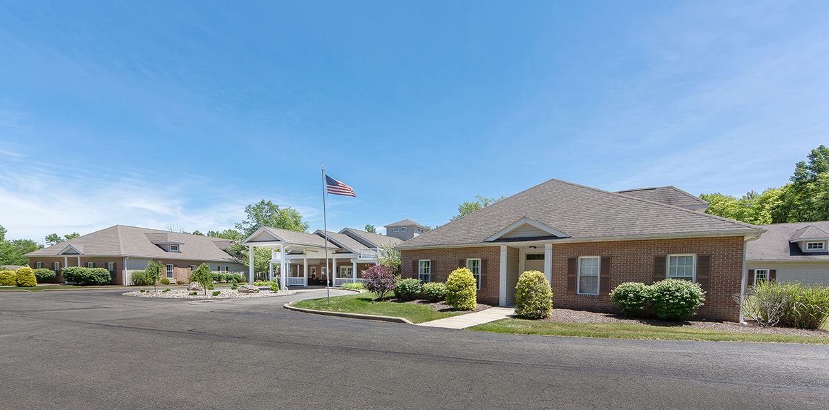 A building with a flagpole flying the American flag, featuring a landscaped entrance and clear blue sky.