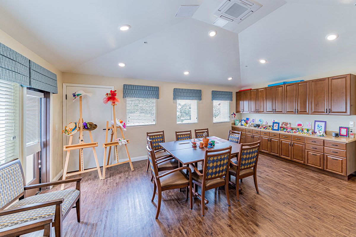 A cozy dining and art area with a wooden floor, table and chairs, kitchenette, and windows.