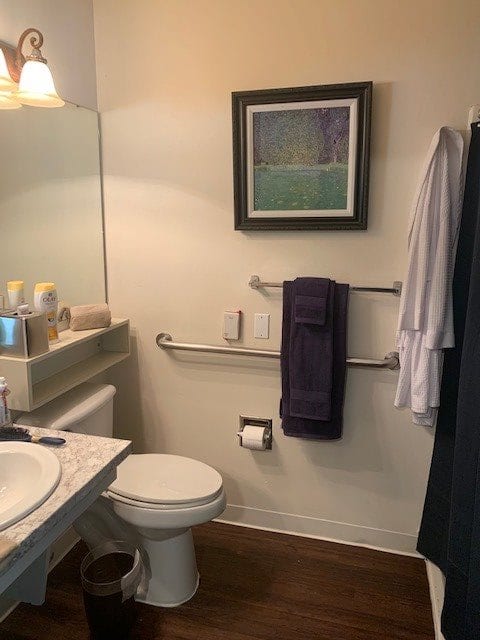 A cozy bathroom with a toilet, sink, and mirror, featuring artwork and neatly arranged towels.