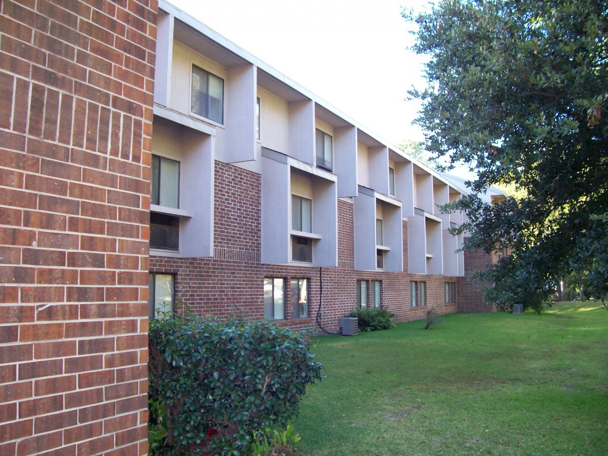 A brick apartment building with multiple floors and a landscaped lawn.