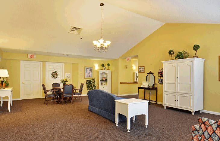 A cozy living room with yellow walls, featuring a blue sofa, dining area, and elegant lighting.