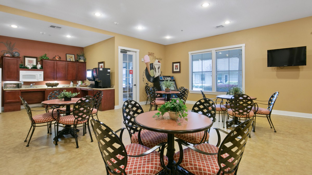 A cozy cafe interior with several round tables and decorative plants.