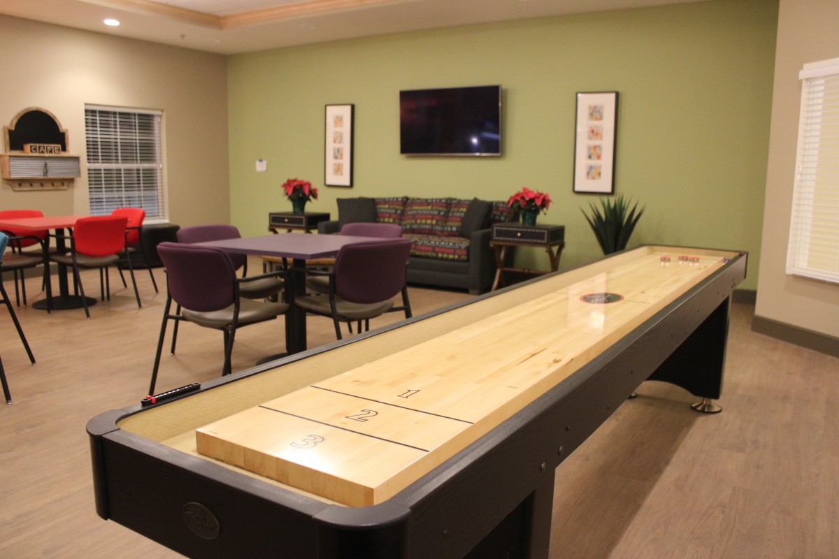 A cozy game room featuring a shuffleboard table, comfortable seating, and a mounted TV on the wall.