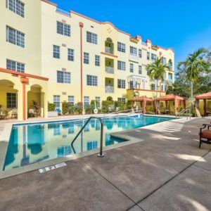 A luxurious apartment complex with a swimming pool and palm trees under a clear blue sky.