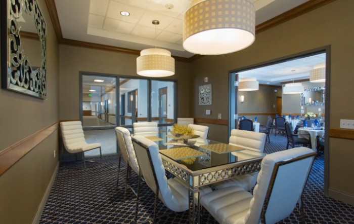 A modern dining room with a glass table, upholstered chairs, and stylish lighting.