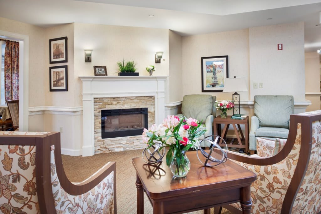 A cozy living room with a fireplace, comfortable seating, floral arrangements, and wall art.