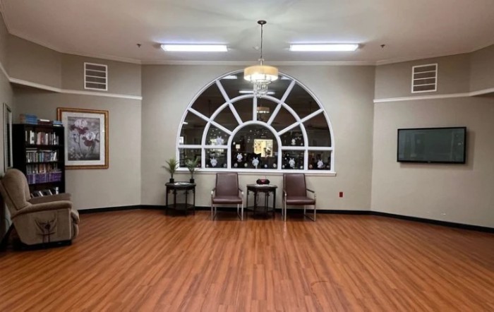 A spacious waiting room with a large arched window, two chairs, and hardwood flooring.