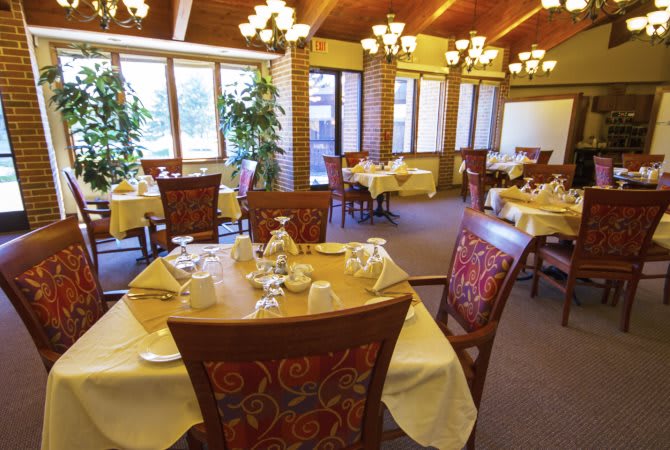 A cozy restaurant interior featuring neatly set tables and comfortable chairs under warm lighting.