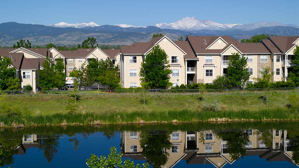 Apartment buildings reflected in a lake with mountains in the background.