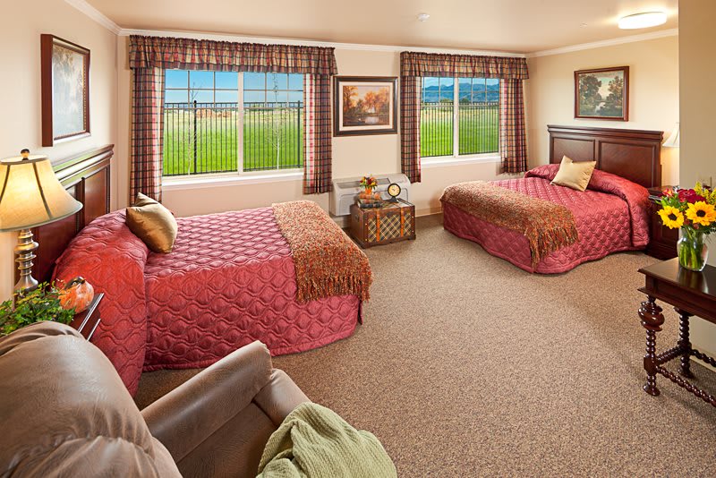 A cozy bedroom with twin beds, decorated in warm tones and featuring large windows with a scenic view.