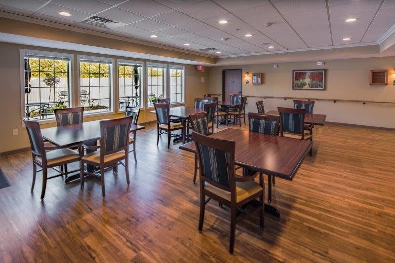 A cozy dining room with wooden tables and chairs, featuring large windows for natural light.