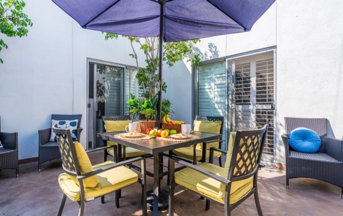 A cozy outdoor patio setup with a table, chairs, and a large umbrella, surrounded by potted plants.