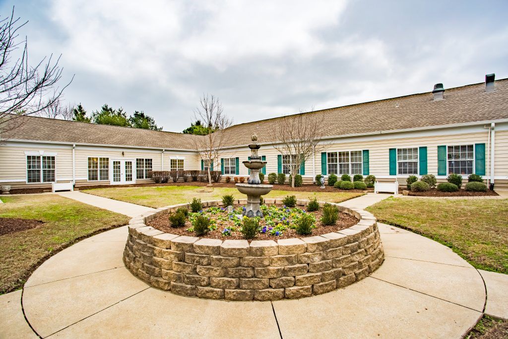 A landscaped courtyard featuring a central fountain surrounded by a well-maintained garden and building.