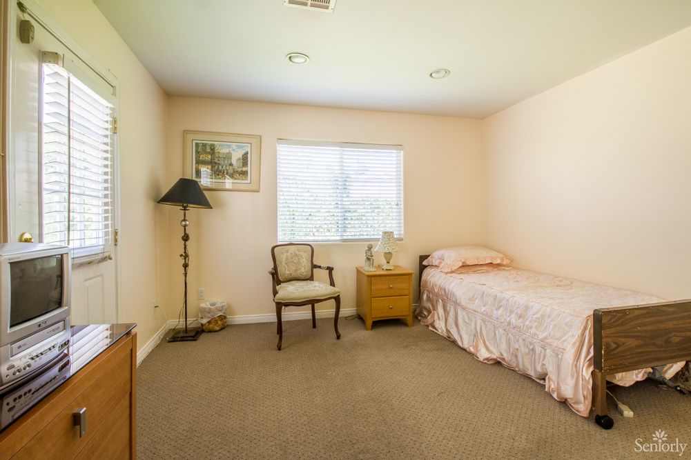 A simple bedroom with a single bed, chair, lamp, and nightstand.