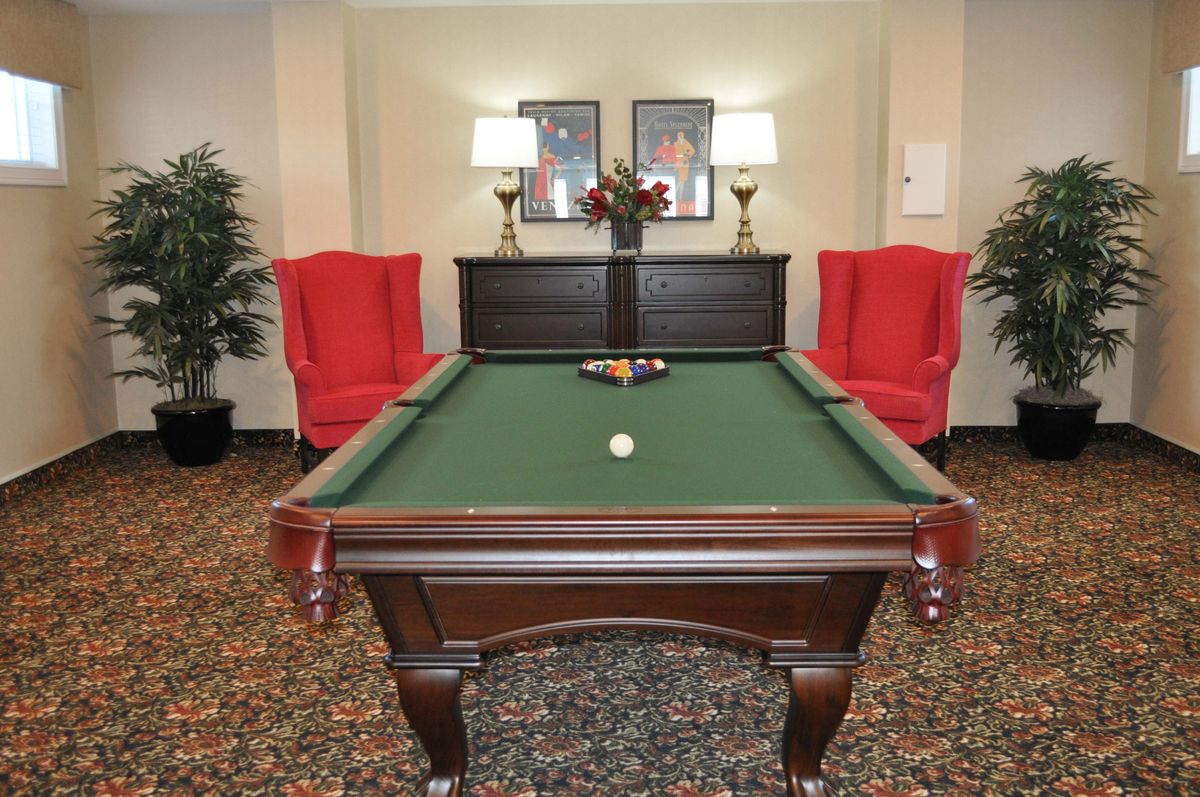 A billiard room with a green pool table, flanked by two red chairs and decorative lamps.
