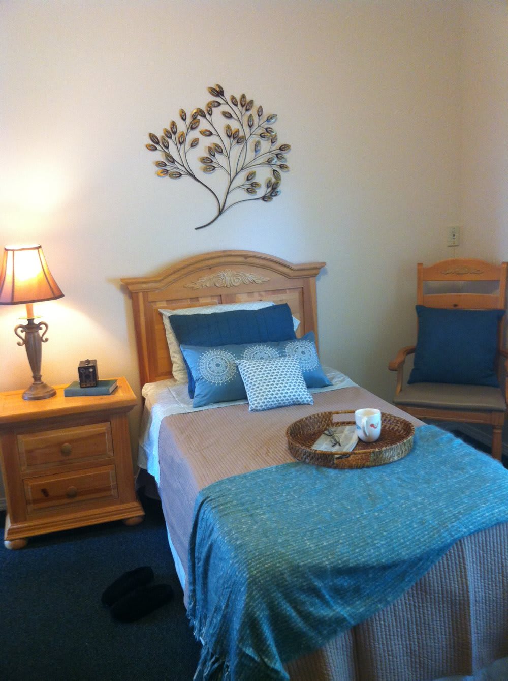 A cozy bedroom with wooden furniture, featuring a bed with decorative pillows, a nightstand with a lamp, and wall art creating a welcoming atmosphere.