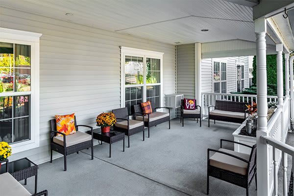 A cozy porch with multiple chairs and a table, decorated with colorful pillows.
