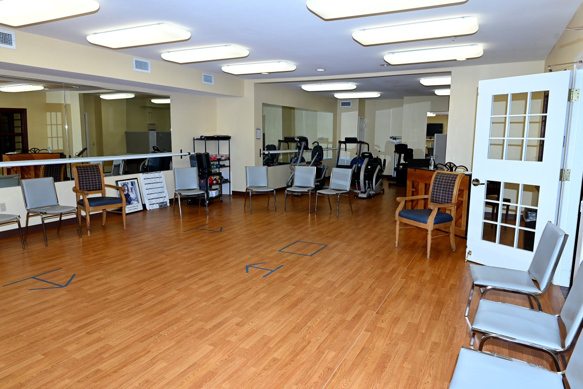 A bright fitness center with exercise equipment and chairs on a hardwood floor, surrounded by mirrors.