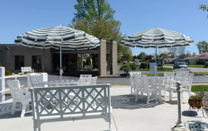 A sunny outdoor patio with white tables and chairs under striped umbrellas.