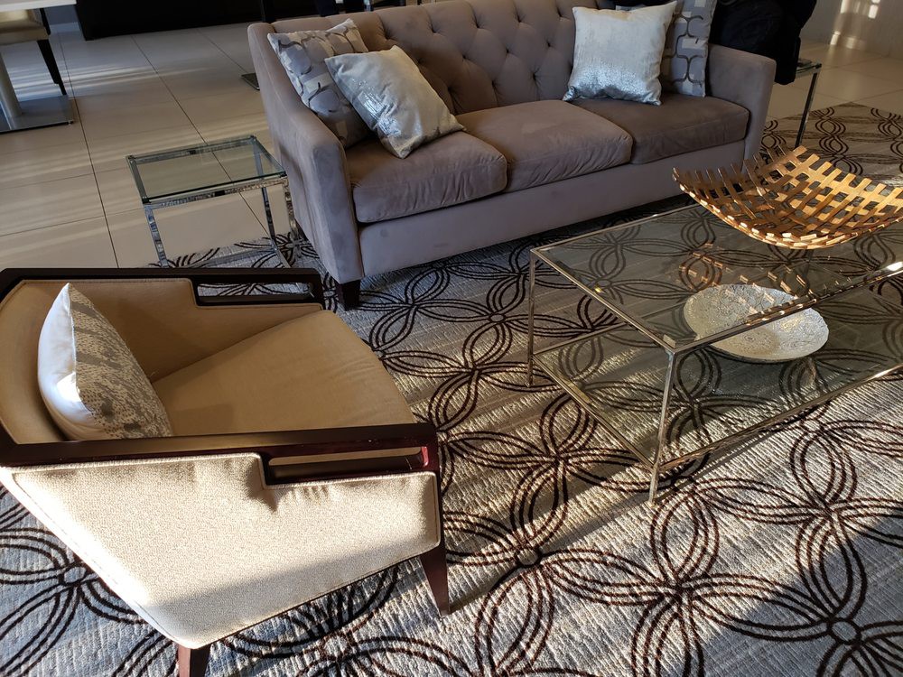A cozy living room with a gray sofa, an armchair, and a glass coffee table on a patterned rug.